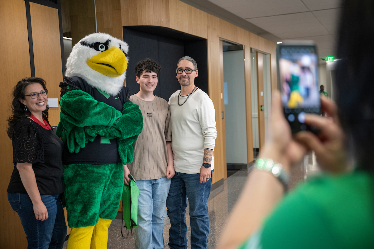 Students and family members pose for a photo with the UNT eagle mascot inside the UNT at Frisco campus while another person takes their picture on a smartphone.